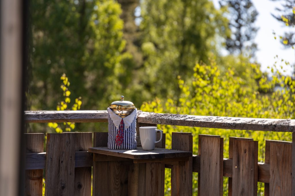 Hot drink and thermos on wooden deck railing, surrounded by sunlit forest