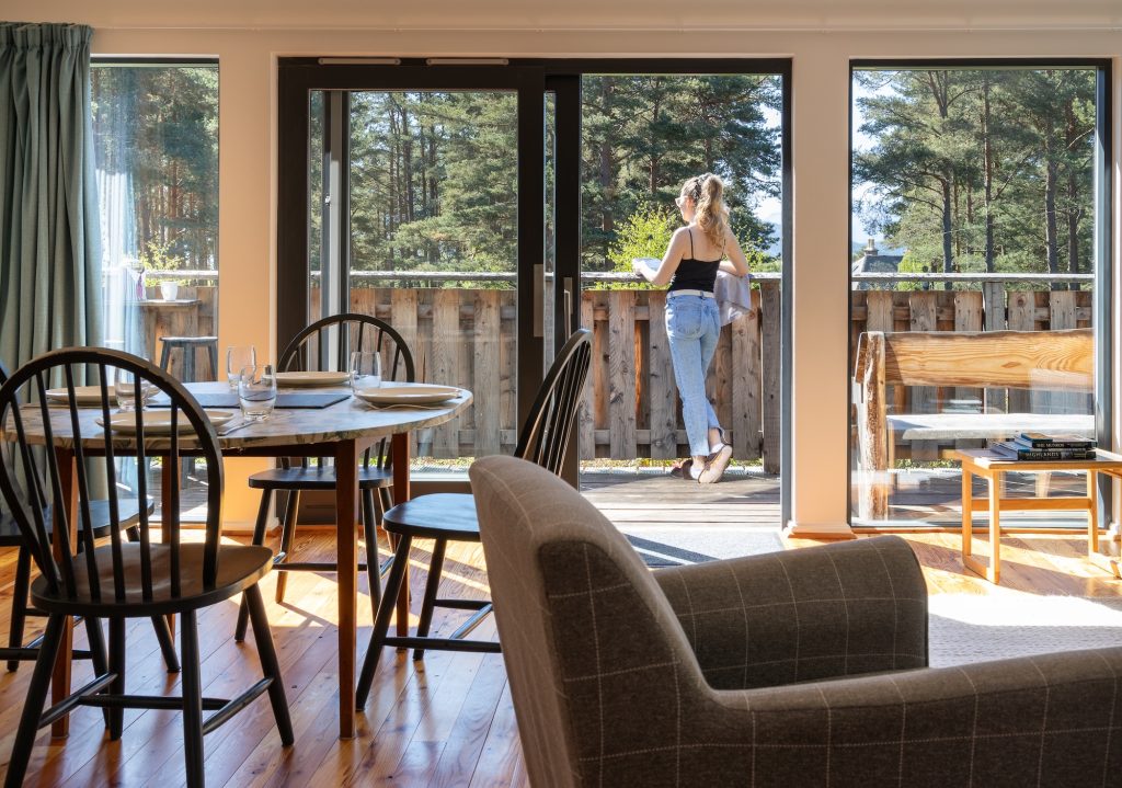 Guest enjoying morning coffee on deck outside cottage with open glass doors