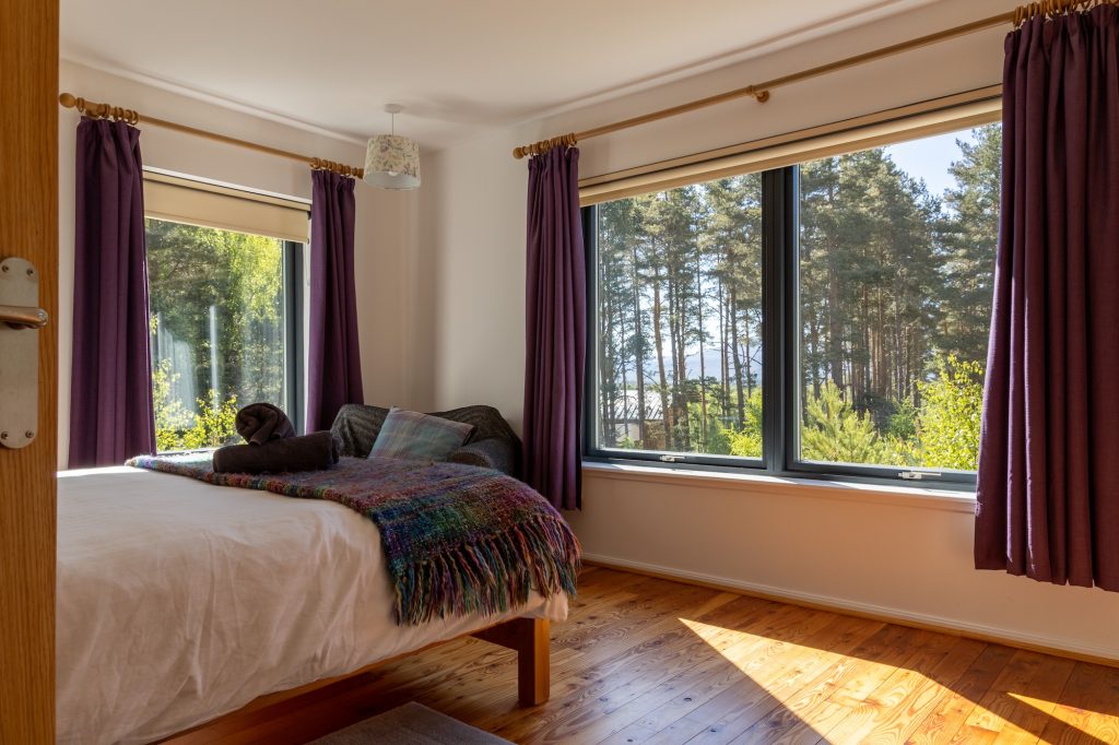Serene bedroom at self-catering Cairngorm Glencoldon Cottage with large windows overlooking the forest