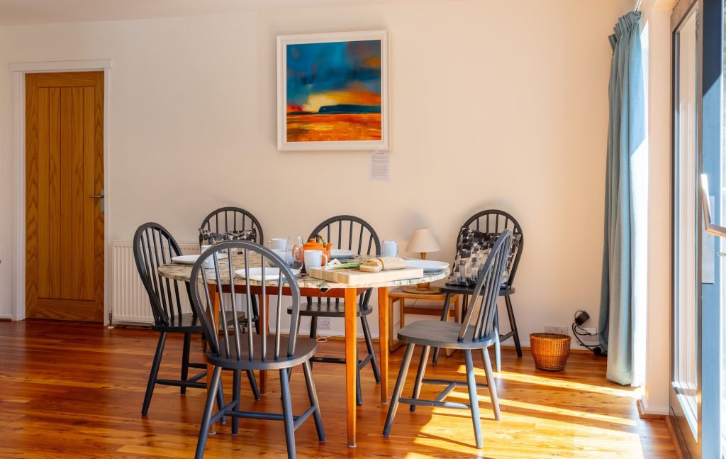 Dining table set for four with Highland artwork and natural light from large window of self catering Cairngorms cottage