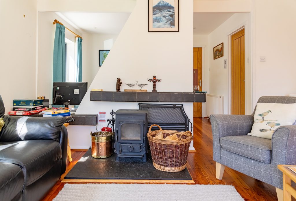 Self-catering Cairngorms Glencoldon Cottage living room with wood-burning stove, books and armchair